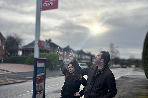 Laura McCarthy and Michael Ward pointing at the 73 bus stop sign